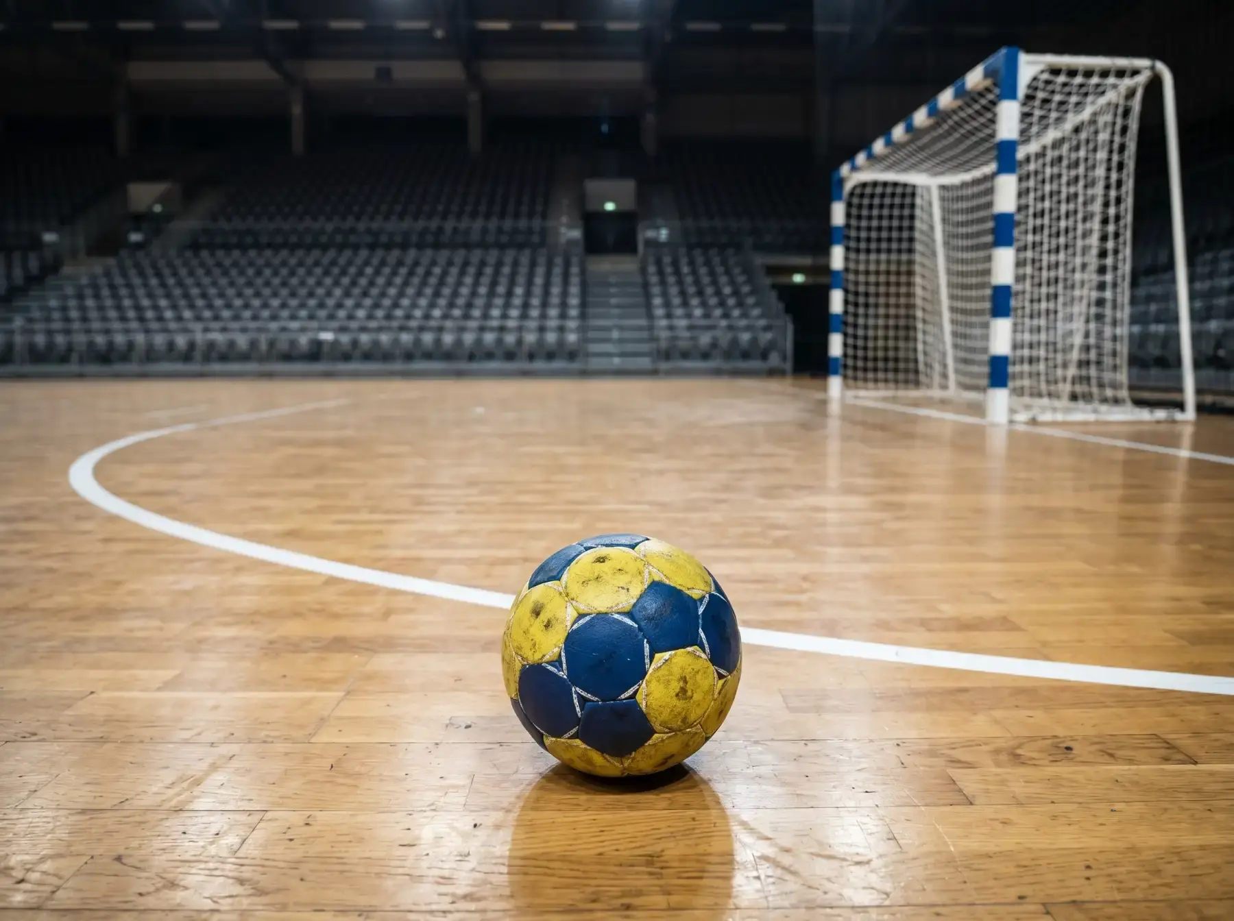 Balón de balonmano reglamentario sobre el parqué de un pabellón profesional con líneas del área visibles